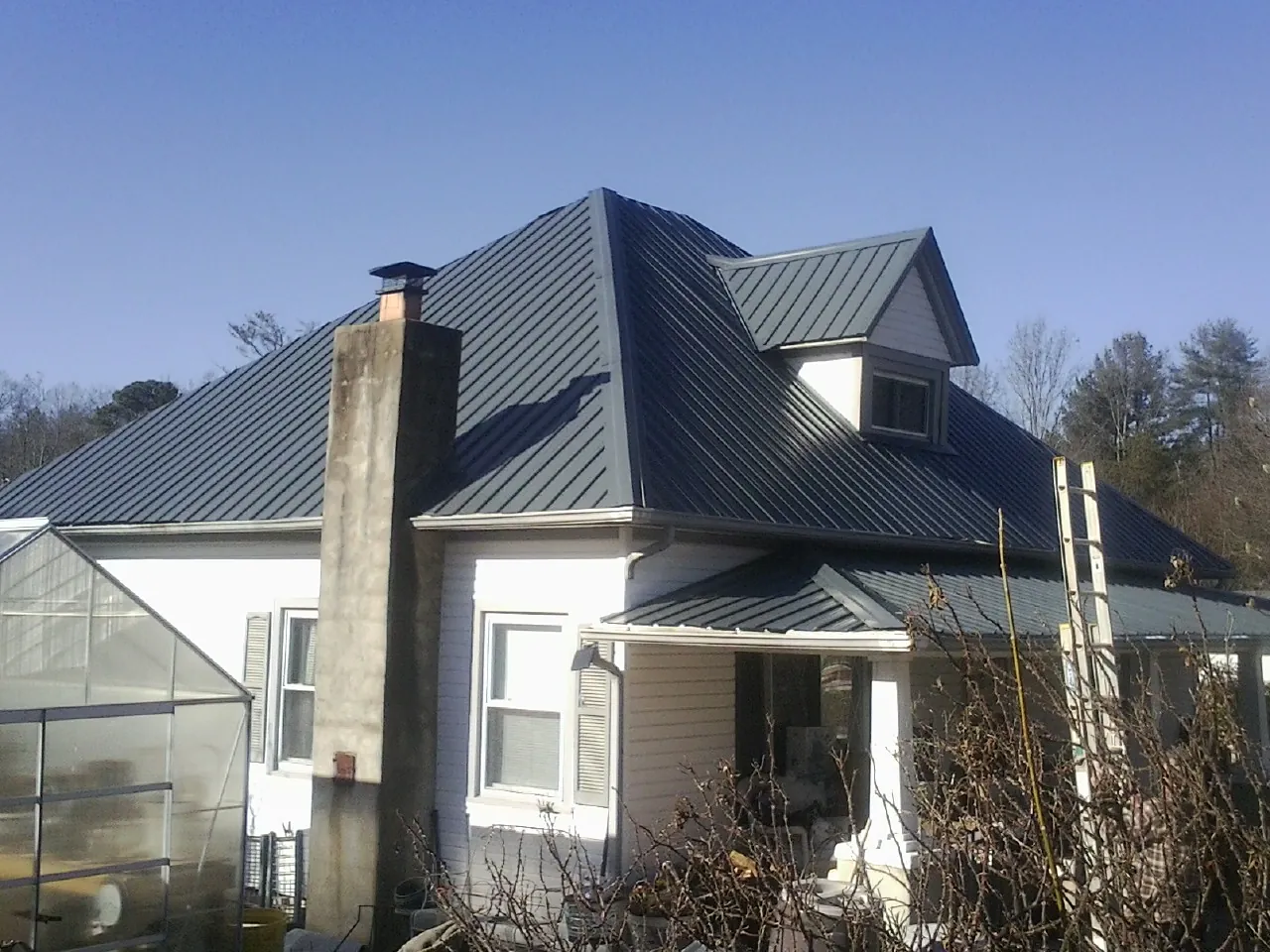 Dark blue standing seam metal roof on a white farmhouse with dormer — Slate & Tile Roof Repair by Roofing Brothers in Goldvein