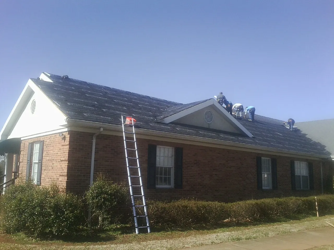 Crew tearing shingles off a brick ranch roof with a ladder set — Emergency Roof Repair work by our crew in Goldvein