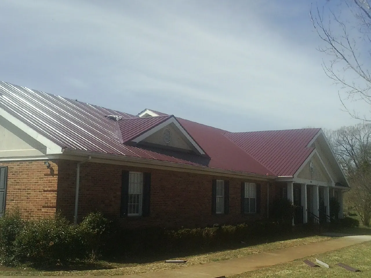 Red metal roof with gabled entries on a long brick building, from a Hail Damage Roof Repair job in Goldvein