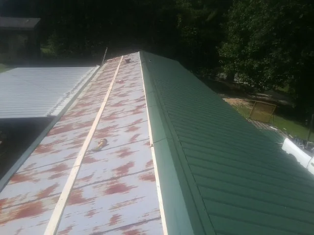 Old rusted panels beside newly installed green metal roofing — Wind Damage Roof Repair by Roofing Brothers in Goldvein