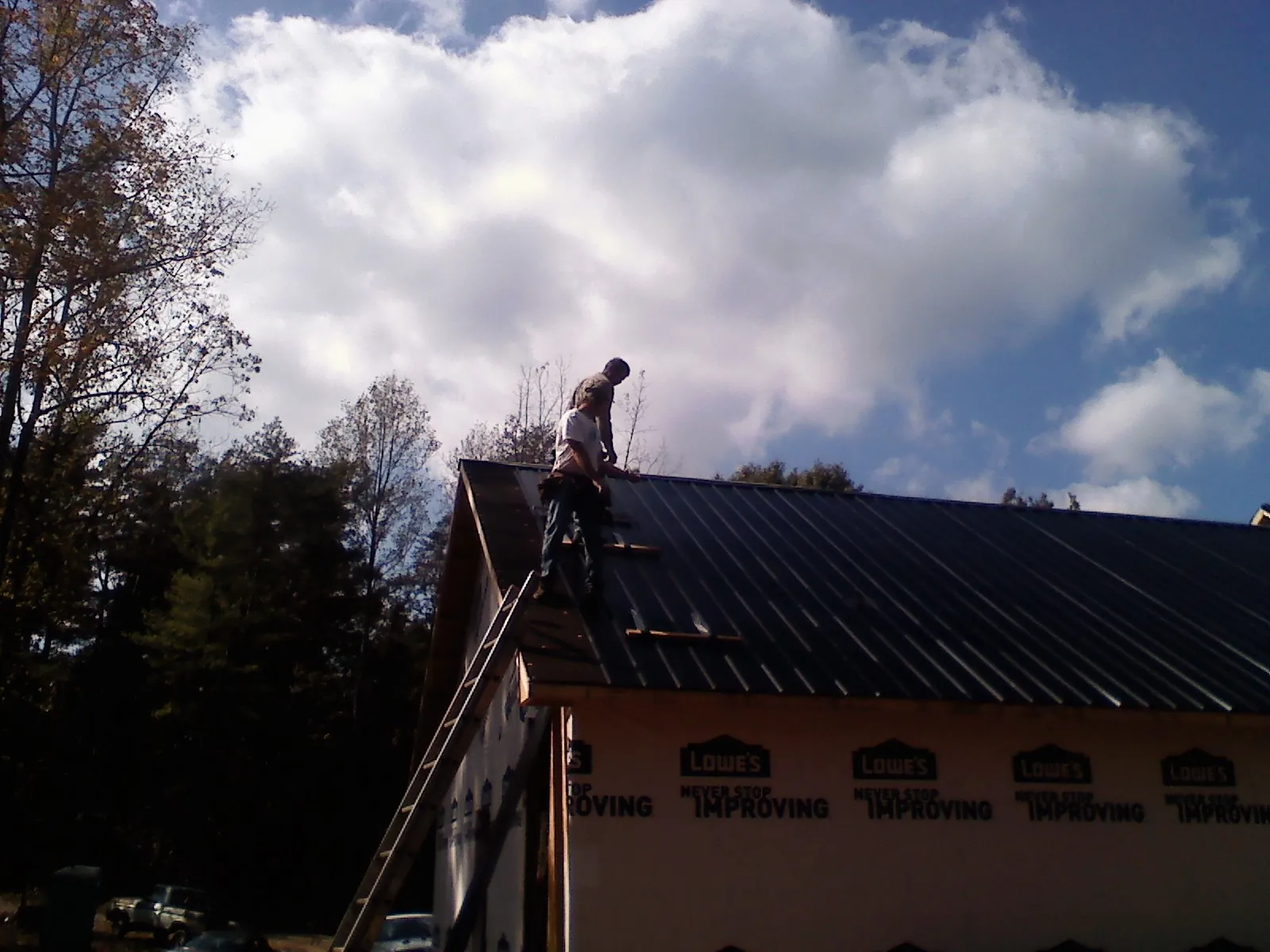Roofer fastening dark metal panels high against a cloudy sky, from a Roof Inspection job in Goldvein