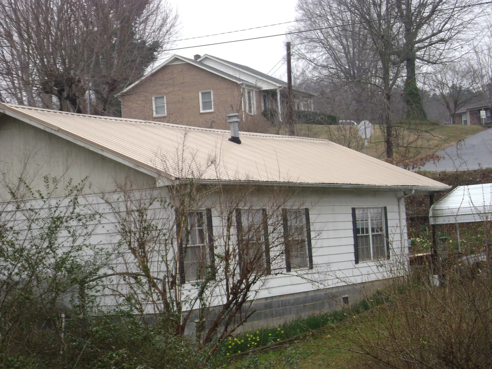 Tan metal roof on a white sided house set into a hillside — Commercial Roofing by Roofing Brothers in Goldvein